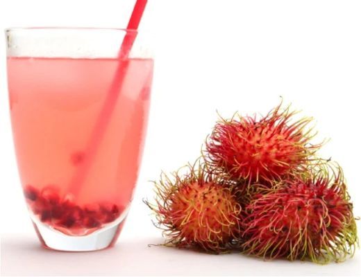 A glass of pink drink with rambutan fruit beside it.