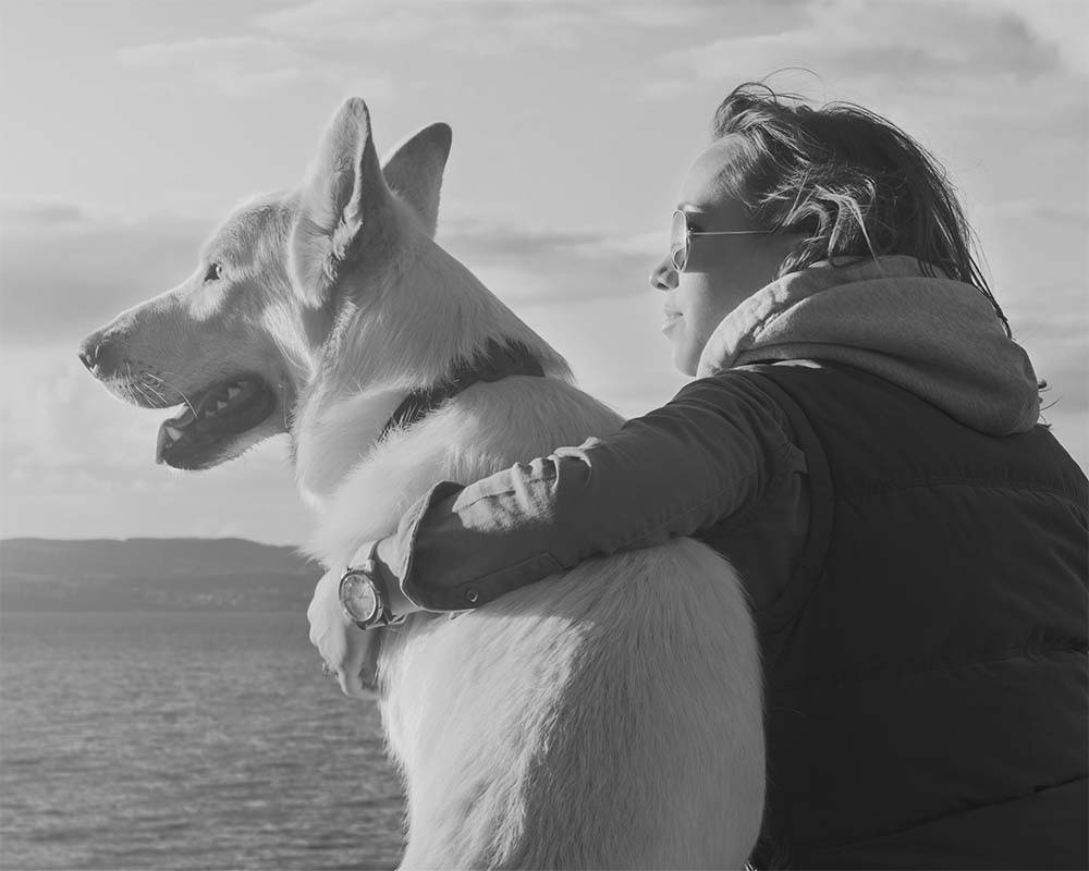 Black and white photo of a woman and her dog looking at horizon