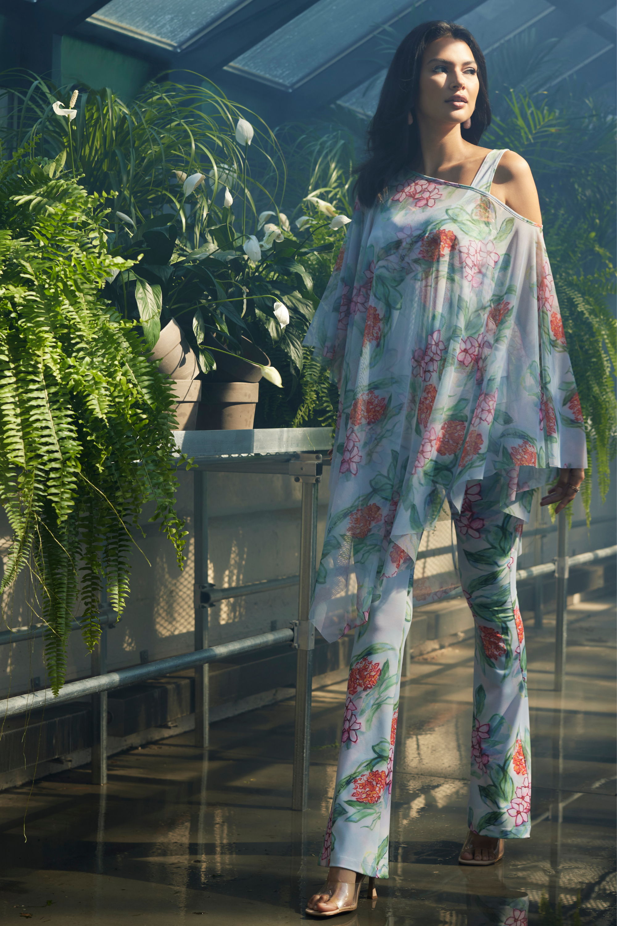 Model wearing floral outfit in a greenhouse surrounded by plants.