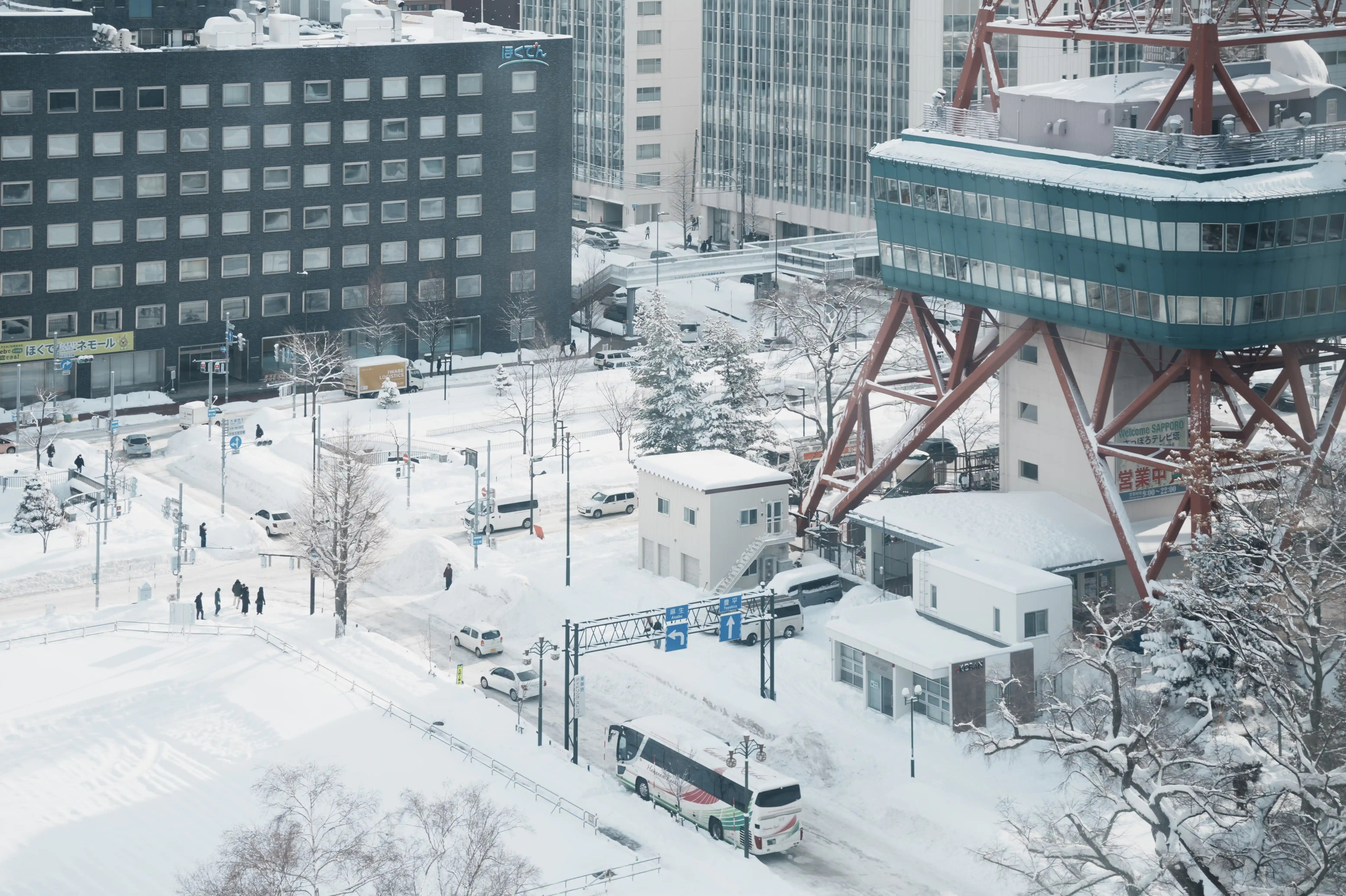 Snow-covered cityscape with buildings, trees, and a bus in winter.