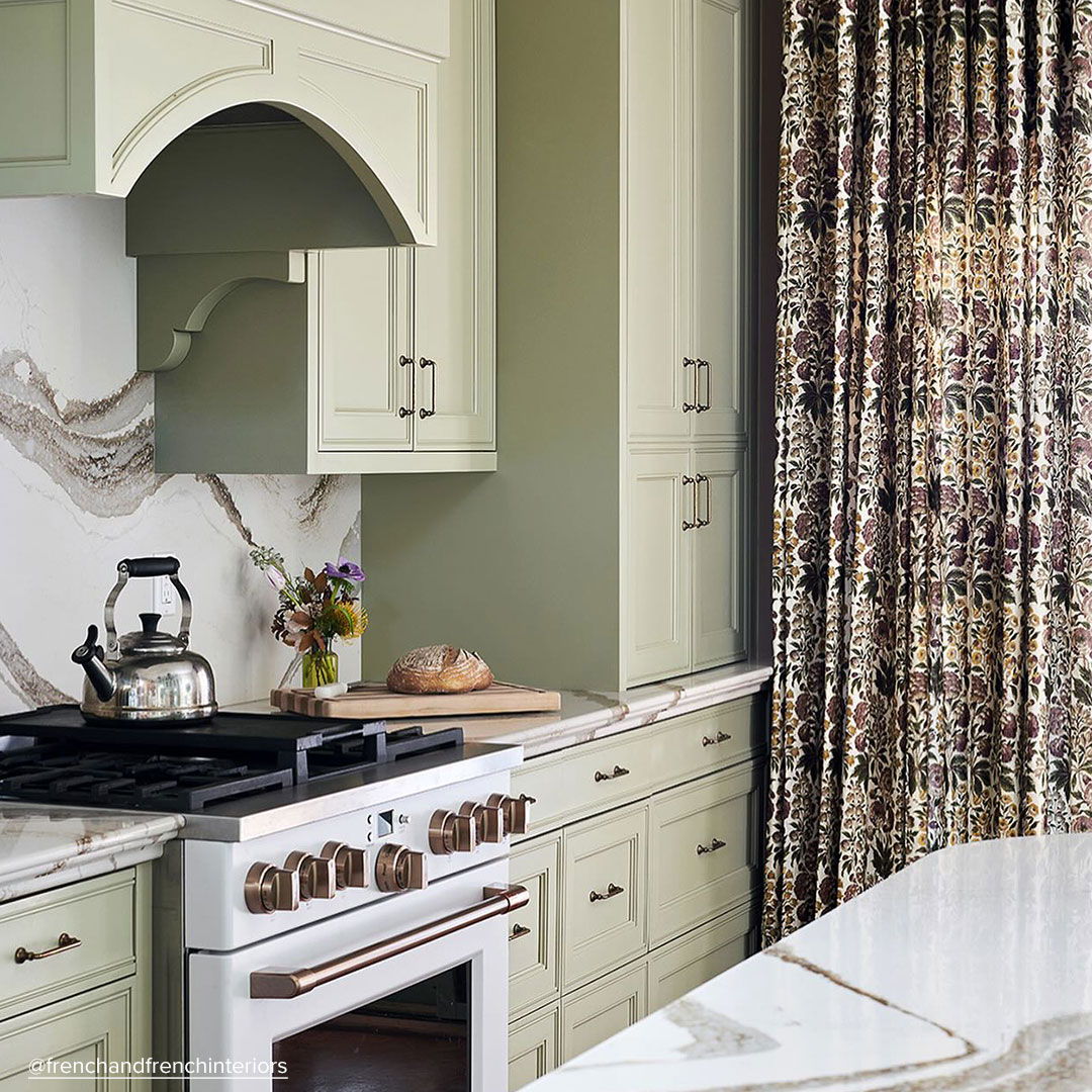 Matte white range in traditional kitchen with green cabinets and patterned curtains.