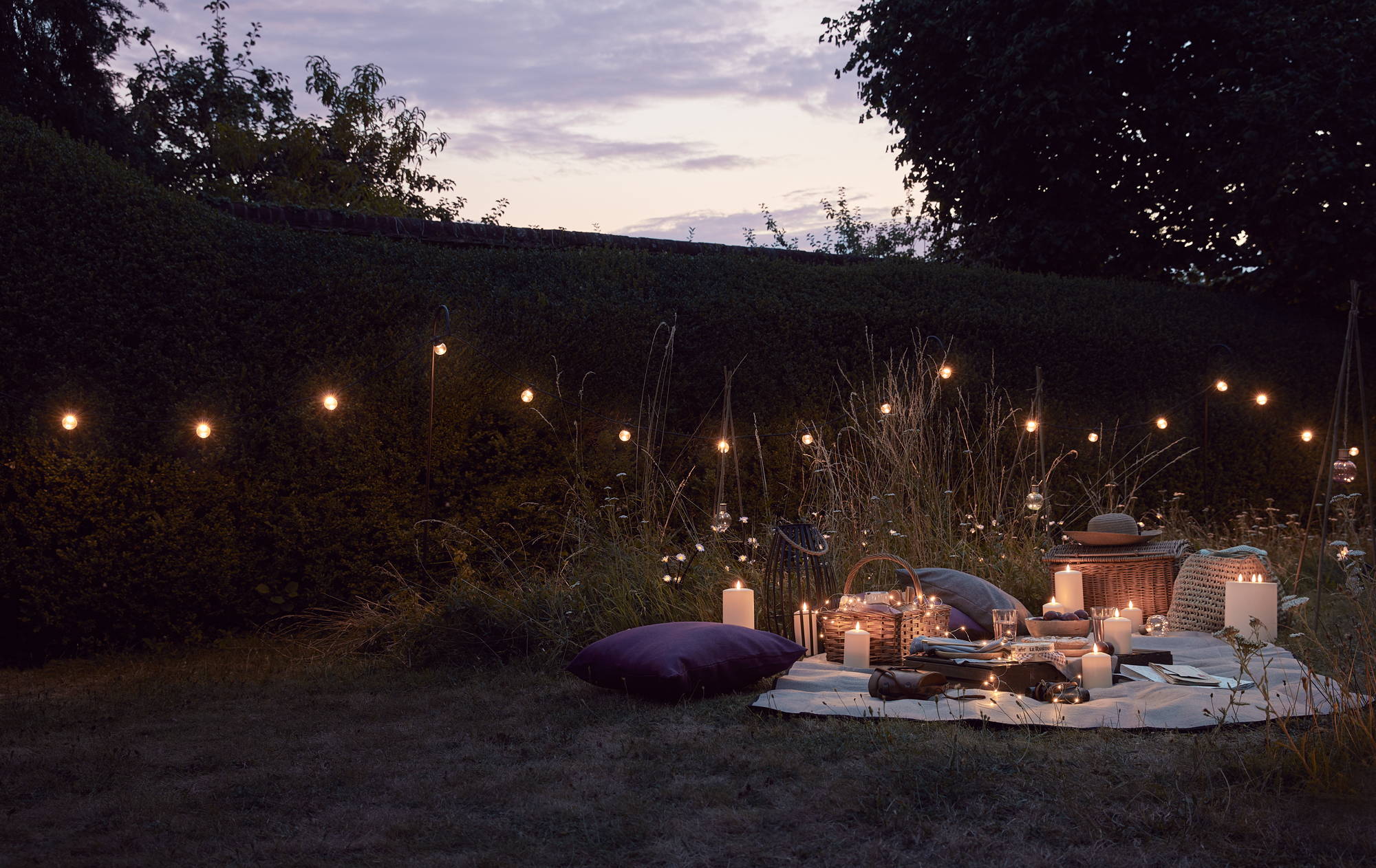 An outdoor night time picnic setting with LED candles, festoon lights and fairy lights.