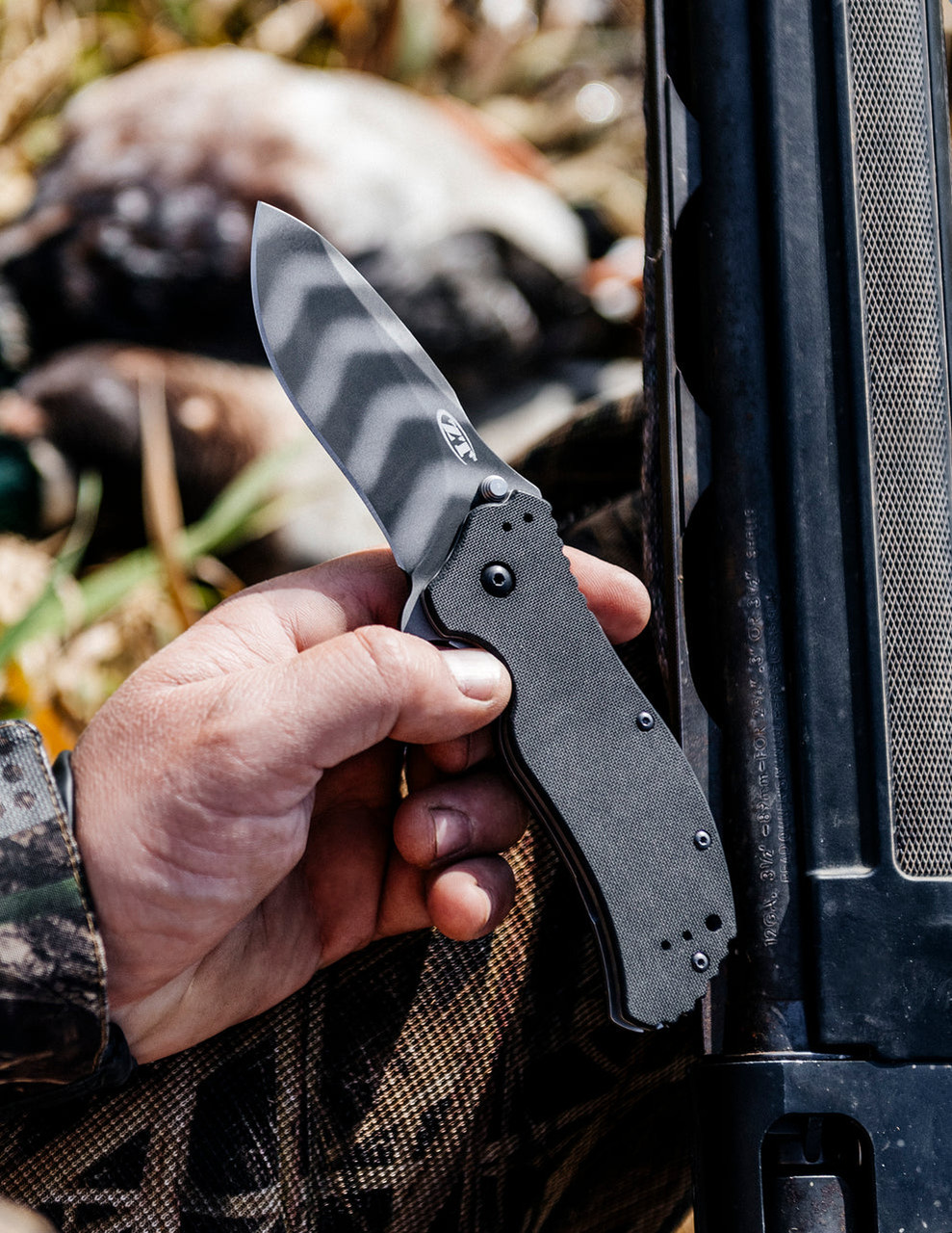 A person holding a folding knife near a hunting scene.