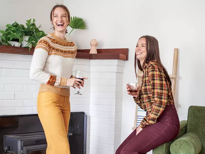Two women laughing inside with drinks in hand.