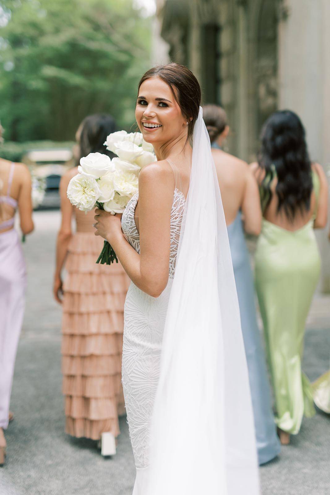 Bride looks back at the camera, showcasing a stunning smile and bouquet