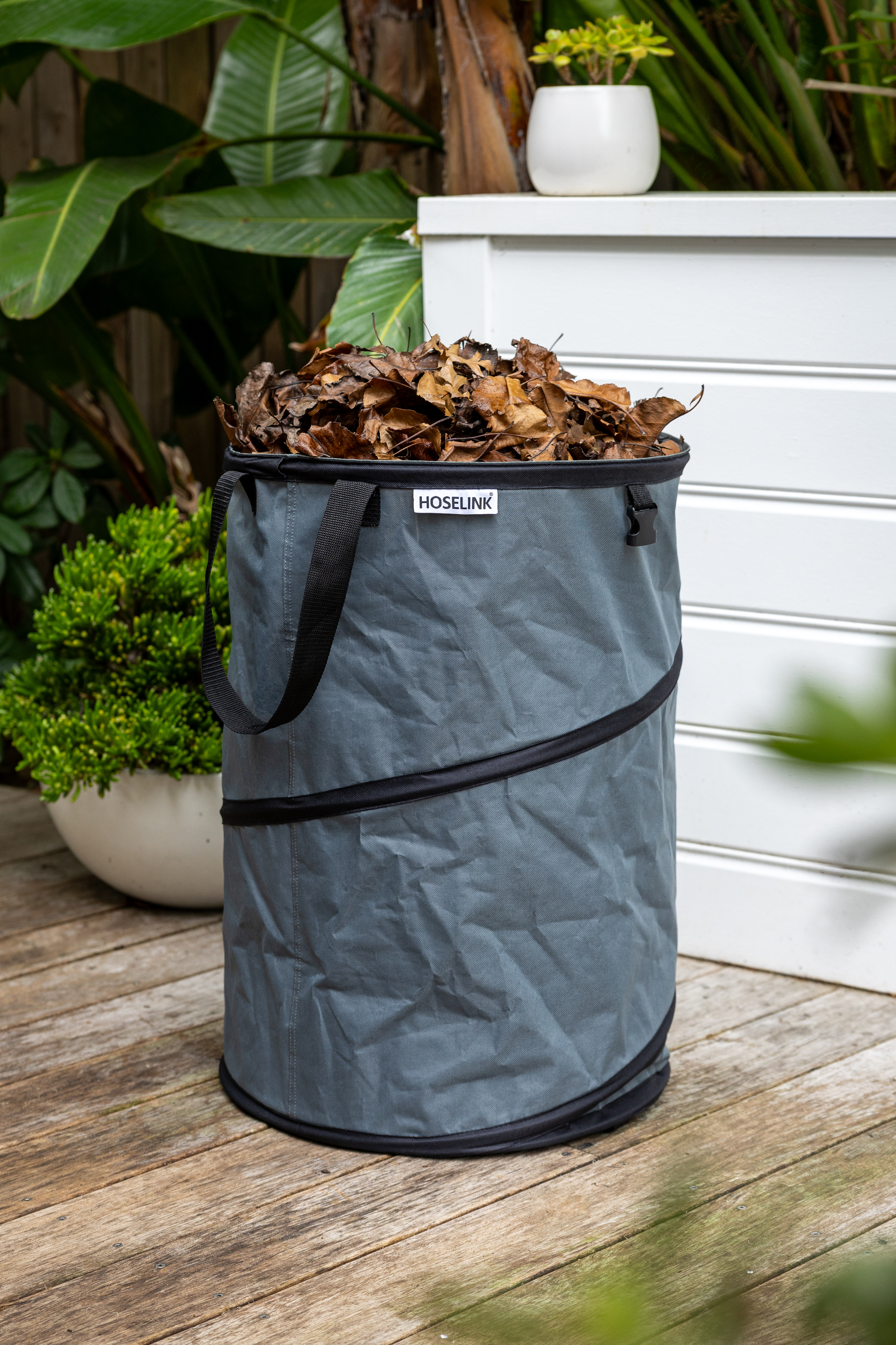 A Hoselink Pop-up Garden Bag filled with leaves, standing on a wooden deck.