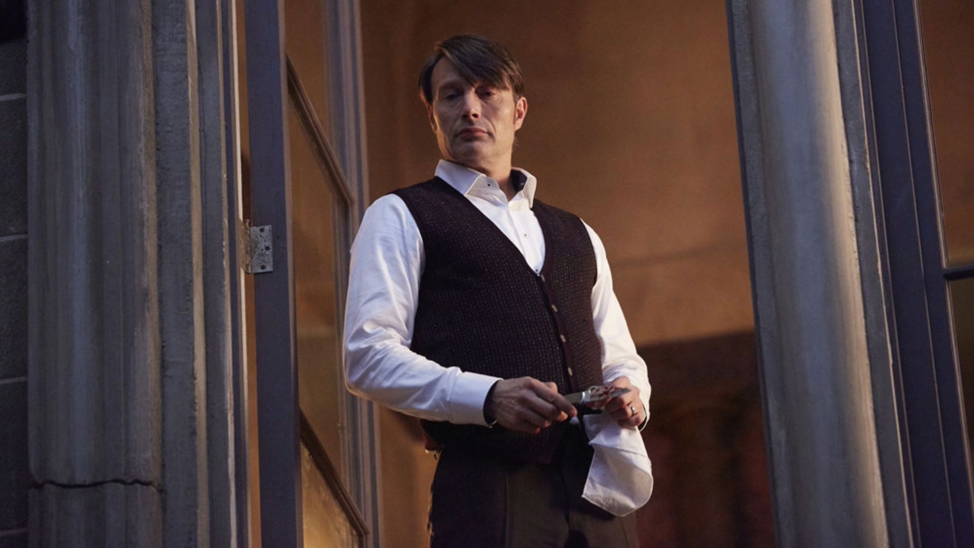 A man in formal attire standing at a doorway, holding an object.
