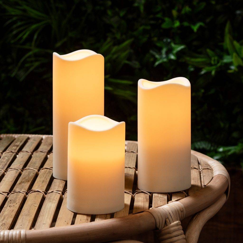 3 LED candles on a wooden table with plants in the background.