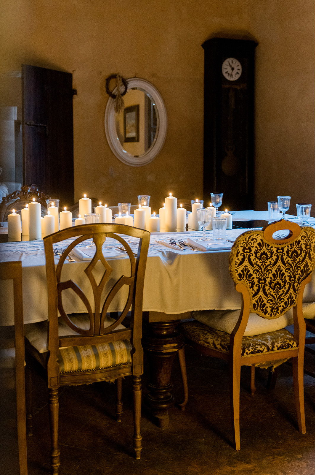 Dining table with candles, two chairs, and a vintage clock in the background.