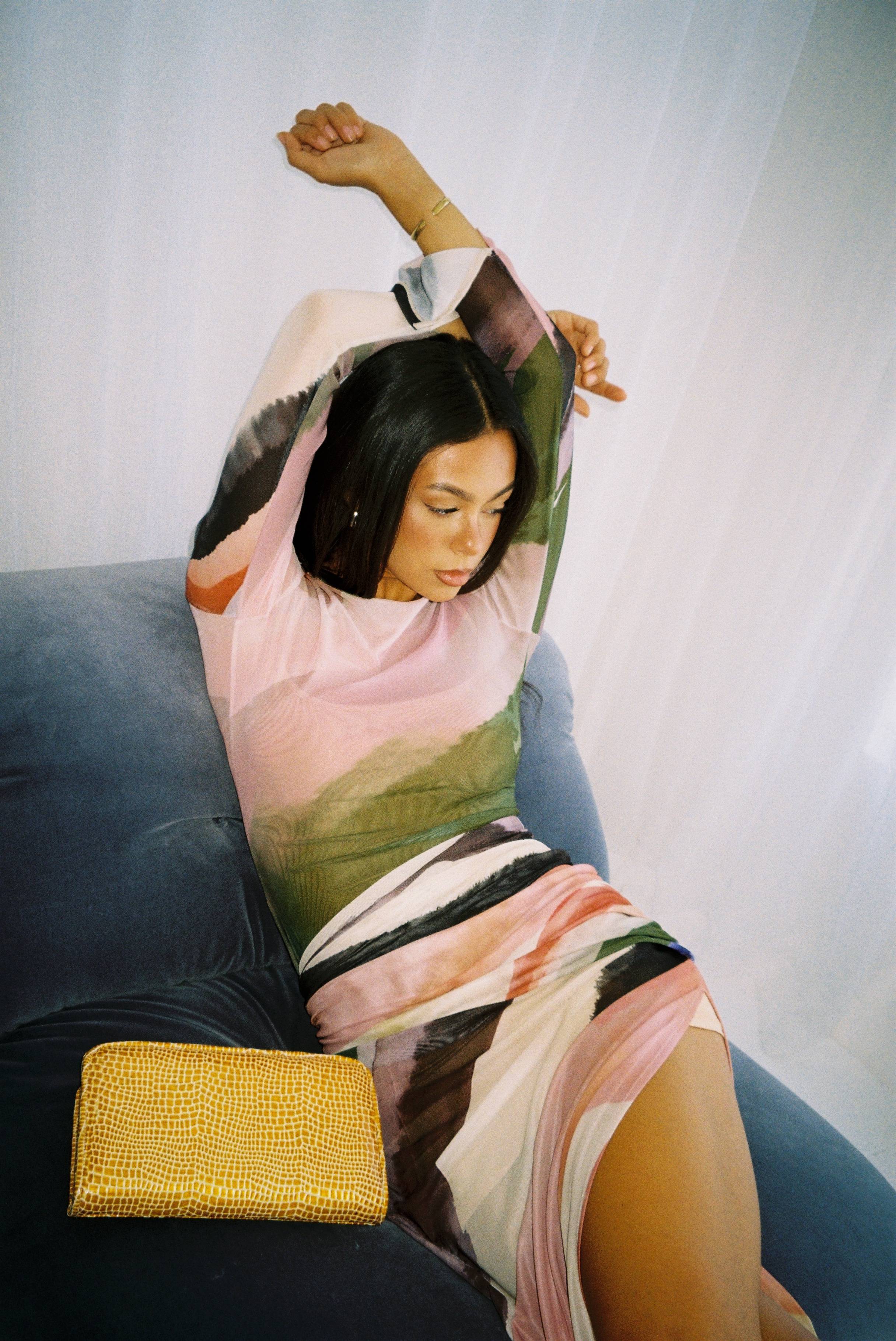 Woman in colorful dress lounging on a couch with a yellow clutch.