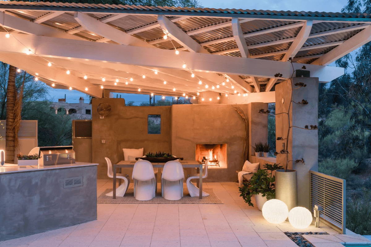 An outdoor kitchen illuminated by string lights, fire place, and glow balls.