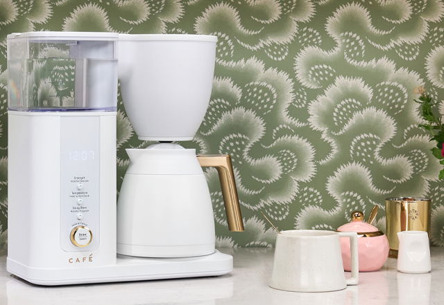 Coffee maker on a countertop with decorative background and cups.