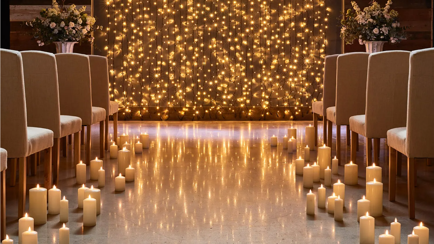 Wedding aisle lined with candles and curtain light illuminating the alter as a backdrop