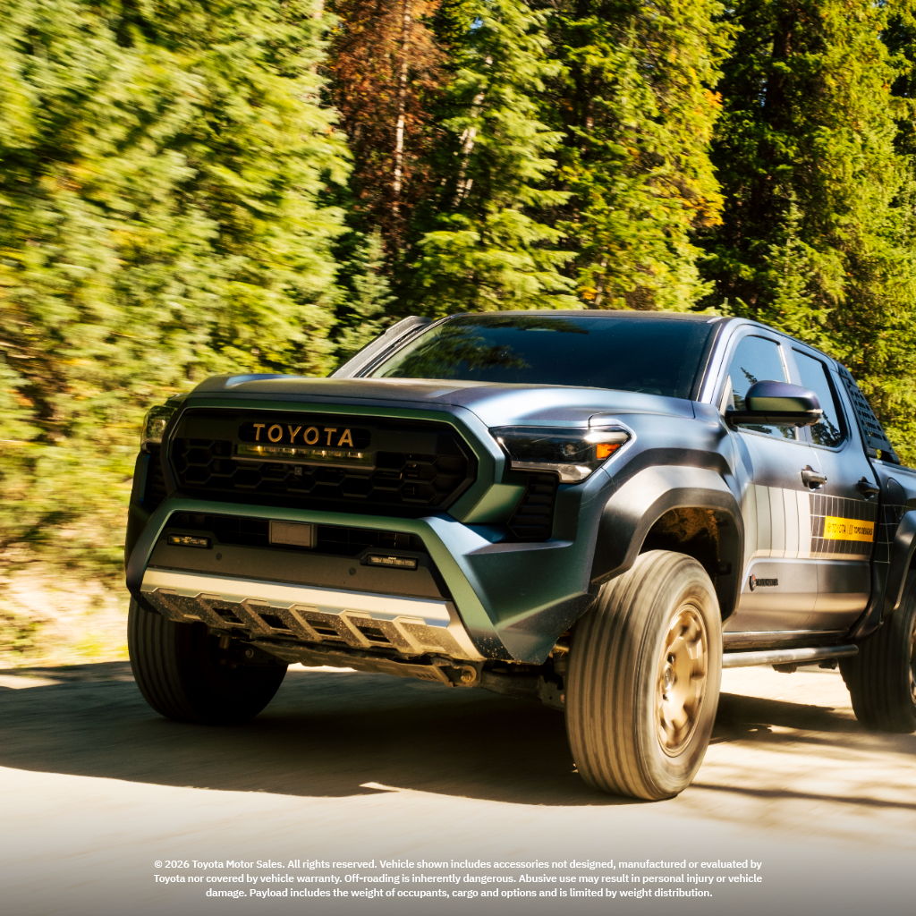 Toyota truck driving on a forest road surrounded by trees.