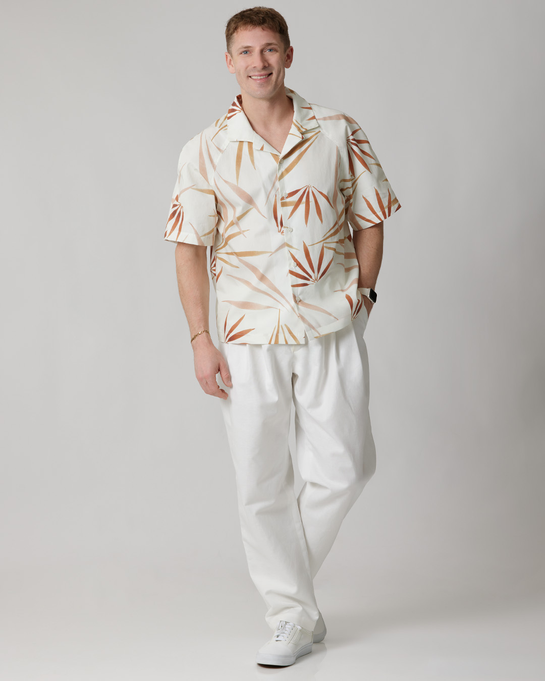 Smiling man in a patterned short-sleeve shirt and white pants.
