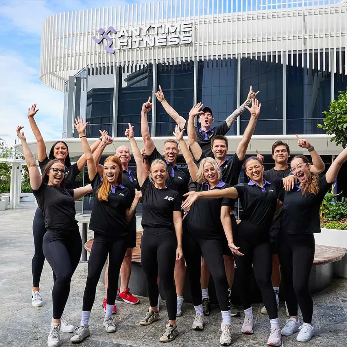 Group of people celebrating outside a fitness center, all wearing matching attire.