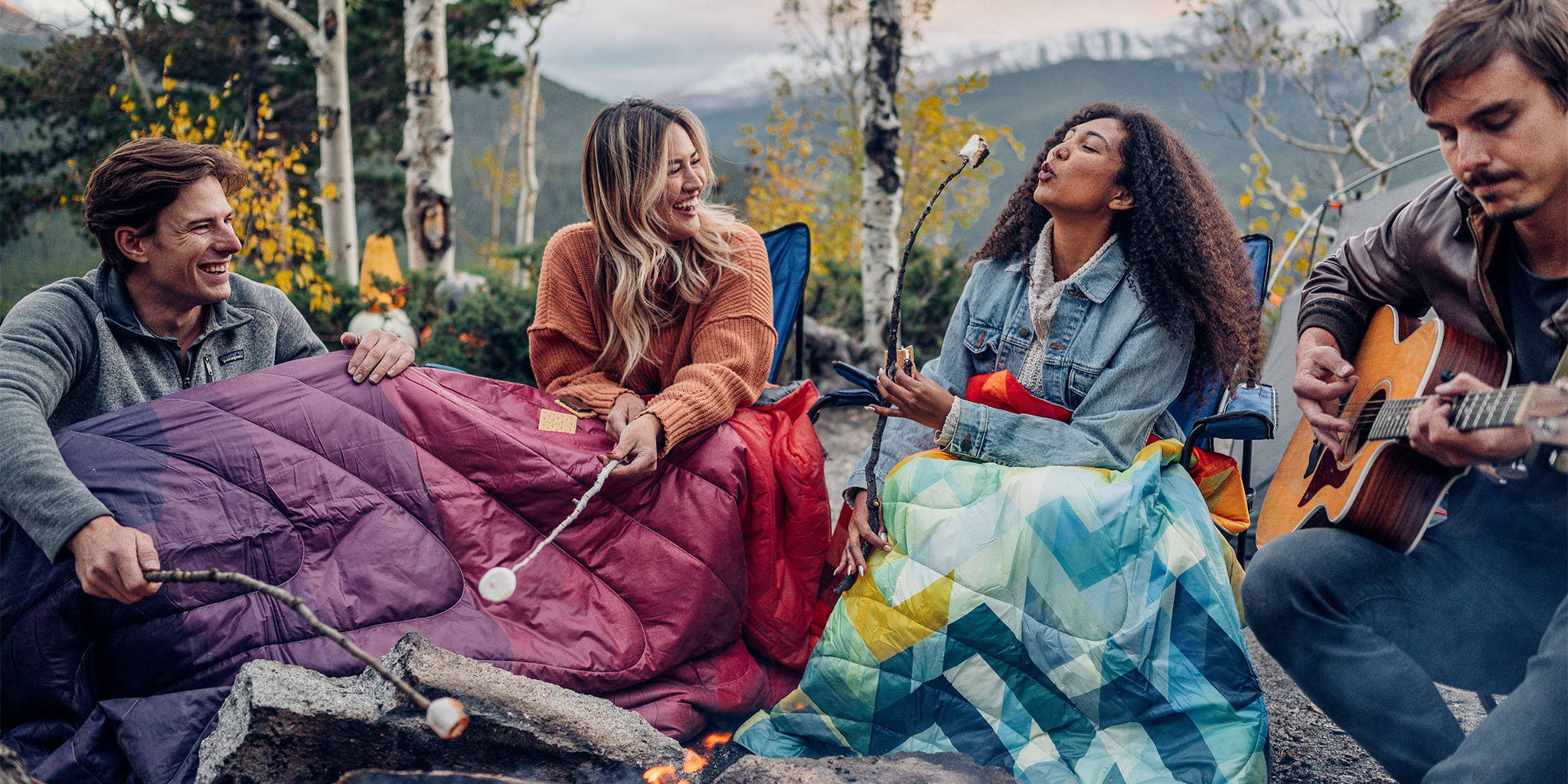 Four friends gathered around a campfire, roasting marshmallows and enjoying their time outdoors with Rumpl blankets to keep them warm.