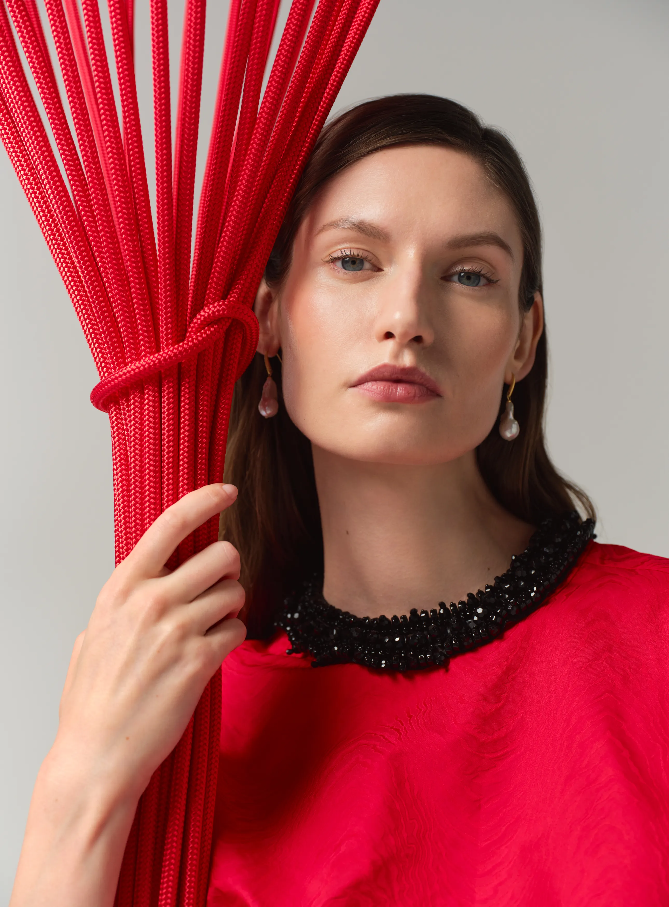A woman in a red dress holding vibrant red ropes.