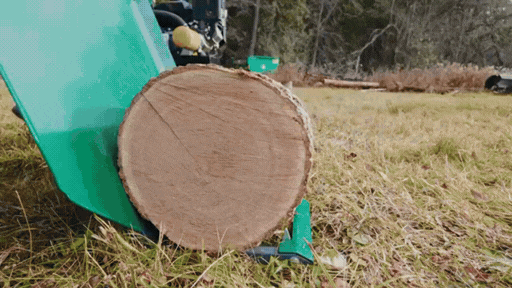 Close-up of a log on grassy ground with machinery in the background.