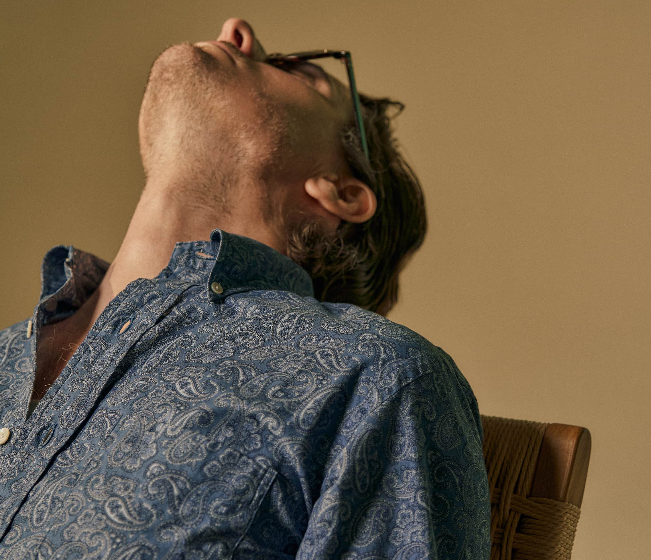 A person with glasses leaning back in a chair, looking upwards.
