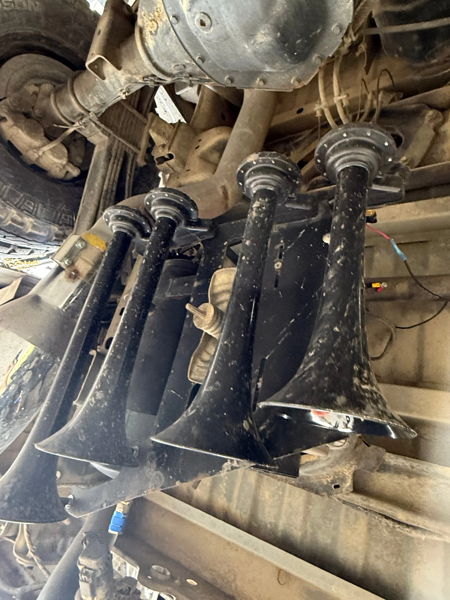 White lifted Ram pickup parked under metal carport during active snowfall with headlights on