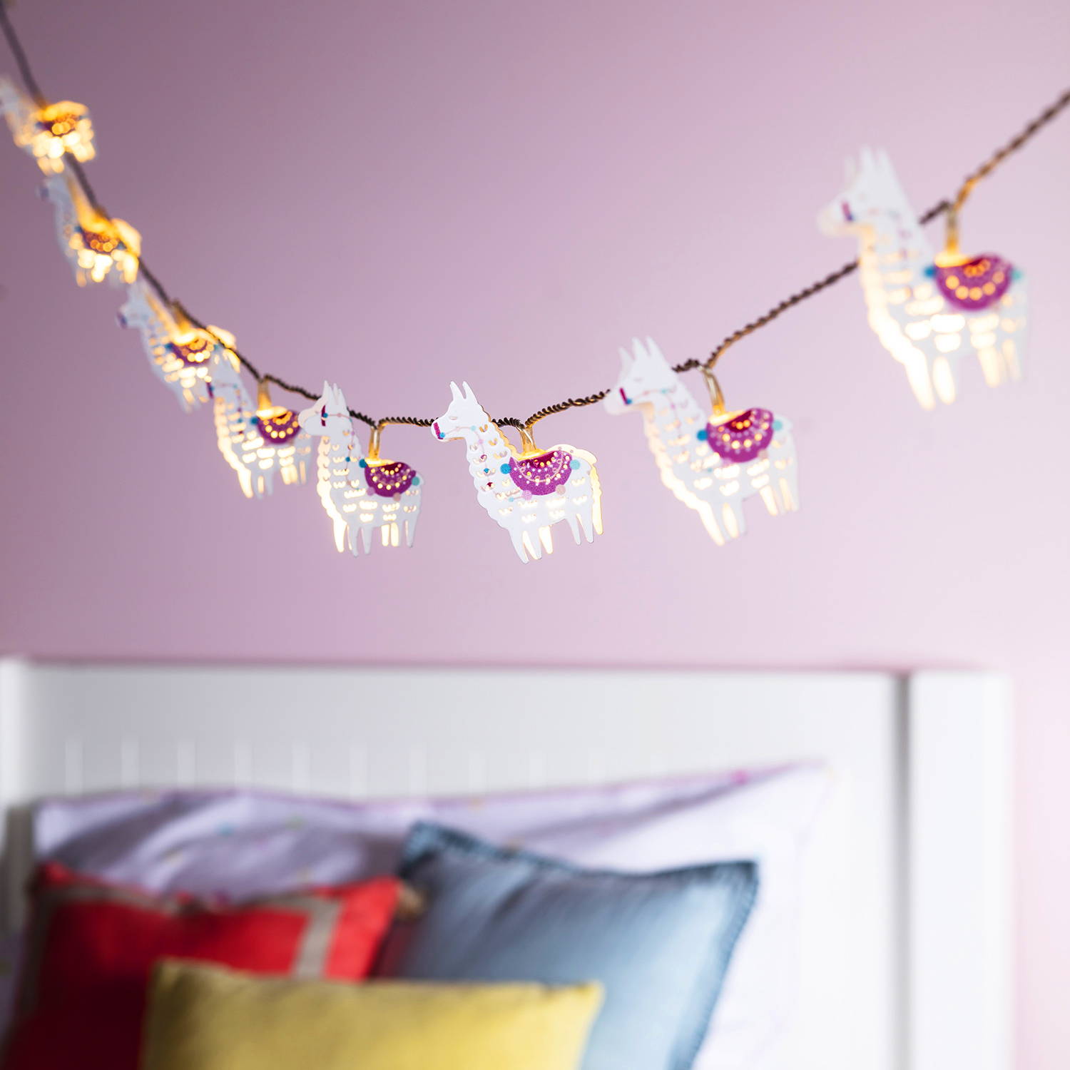Llama fairy lights hanging in a bedroom with a pink wall.