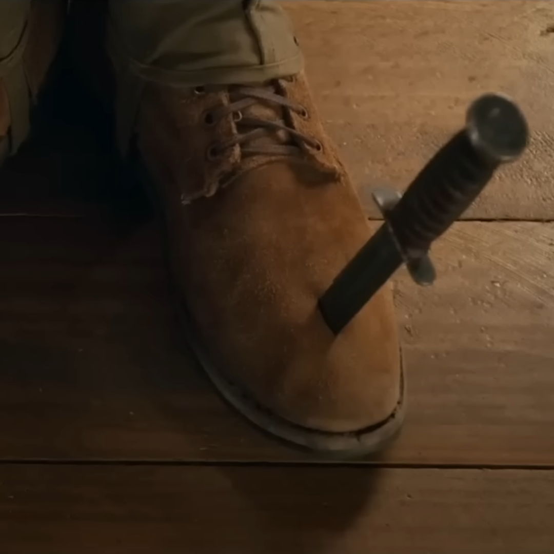 A shoe with a dagger stabbed into it on a wooden floor.