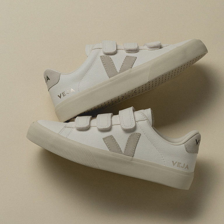 White sneakers with Velcro straps on a beige background.