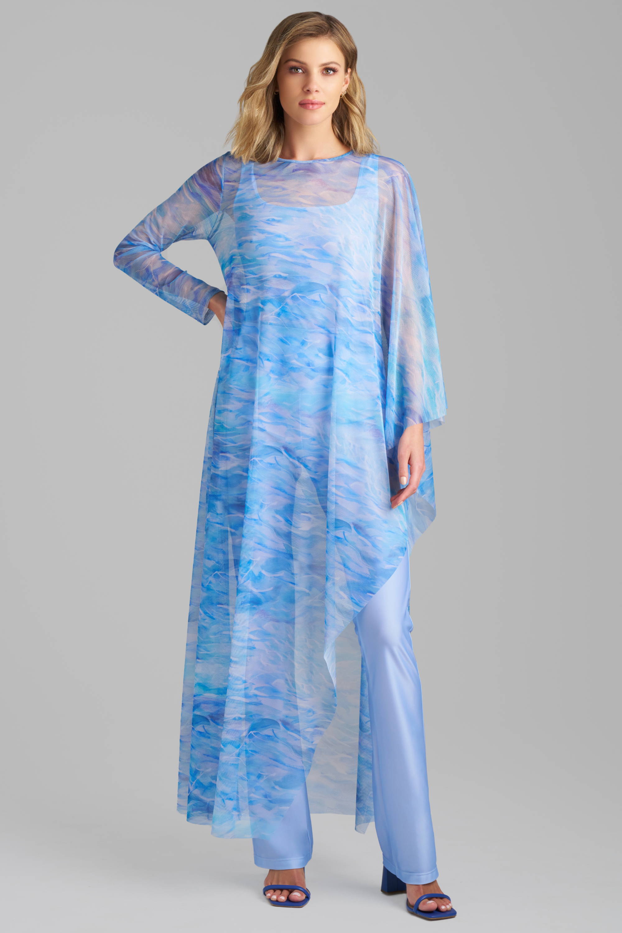 Woman wearing blue mesh kaftan poncho cover up over periwinkle stretch knit tank top and pants by Ala von Auersperg
