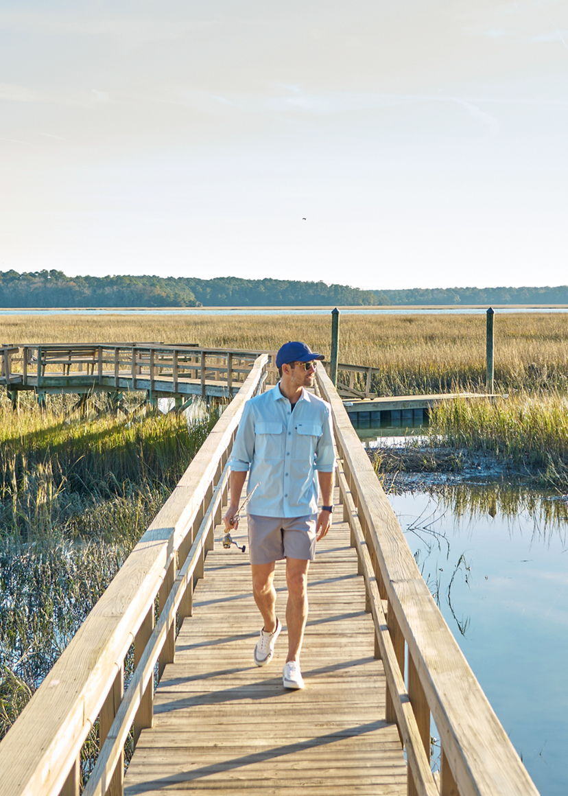 A person walking on a wooden boardwalk by a marshy area.