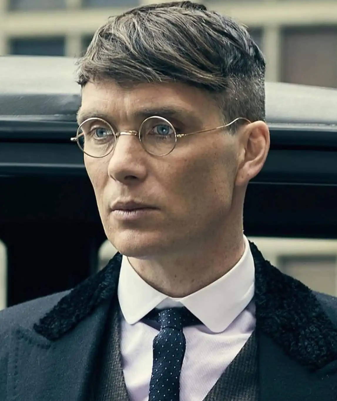 Cillian Murphy wearing retro round eyeglasses in Peaky Blinders with a grey suit and a black coat