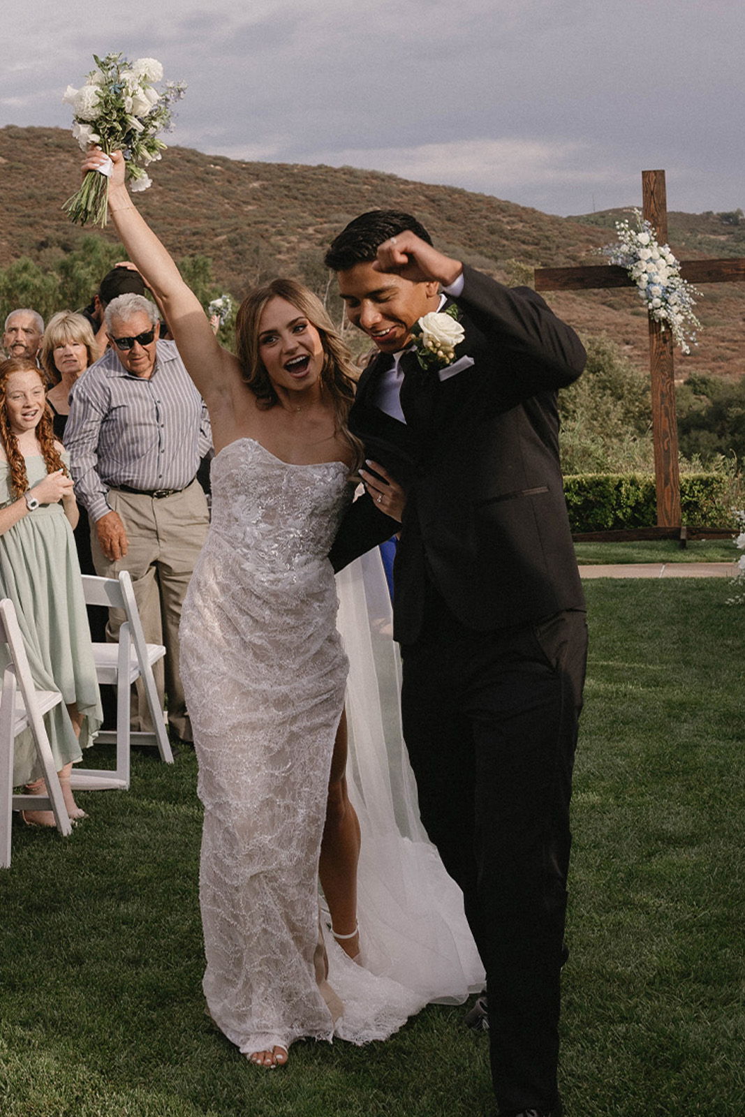 Bride and groom celebrating at their wedding ceremony with guests in background.