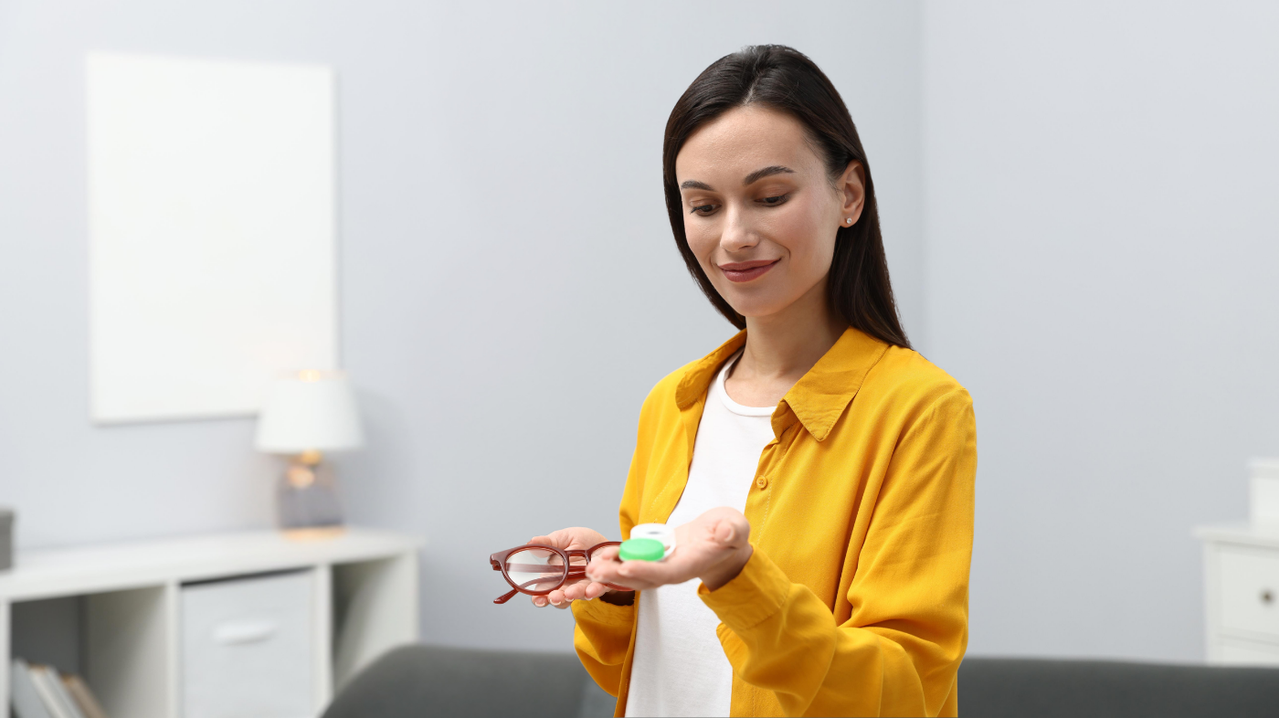 Person holding prescription reading glasses alongside a contact lens case, illustrating vision correction options and proper contact lens storage and eye care routine
