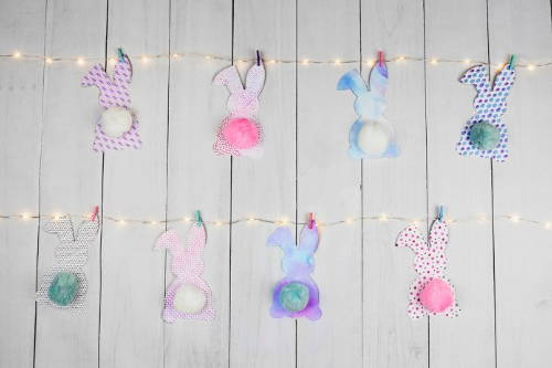 Easter bunny garland with some fairy lights against a neutral wooden background.