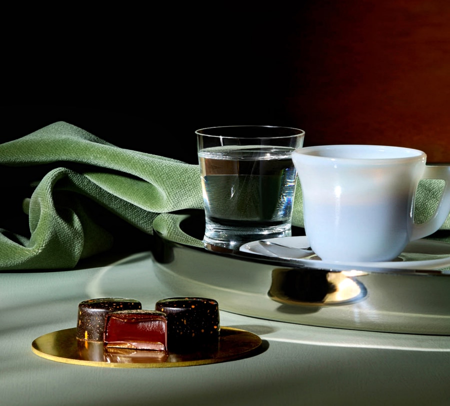 Coffee cups on a silver tray with candies and a green cloth.