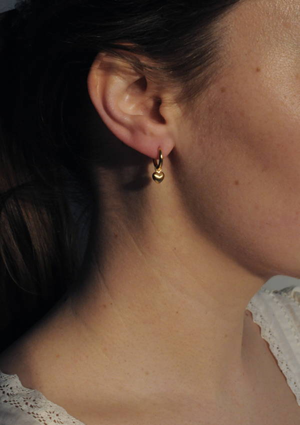 A close up of a model wearing a heart pendent hoop earring.