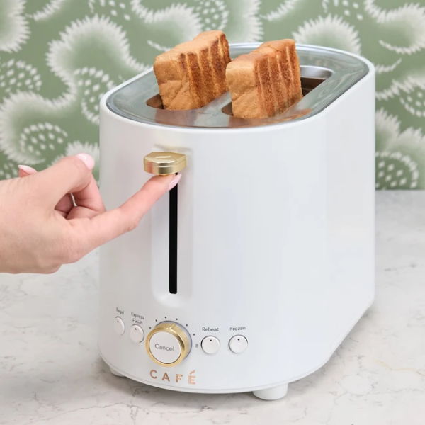 A hand pressing the lever of a white toaster with two slices of bread.