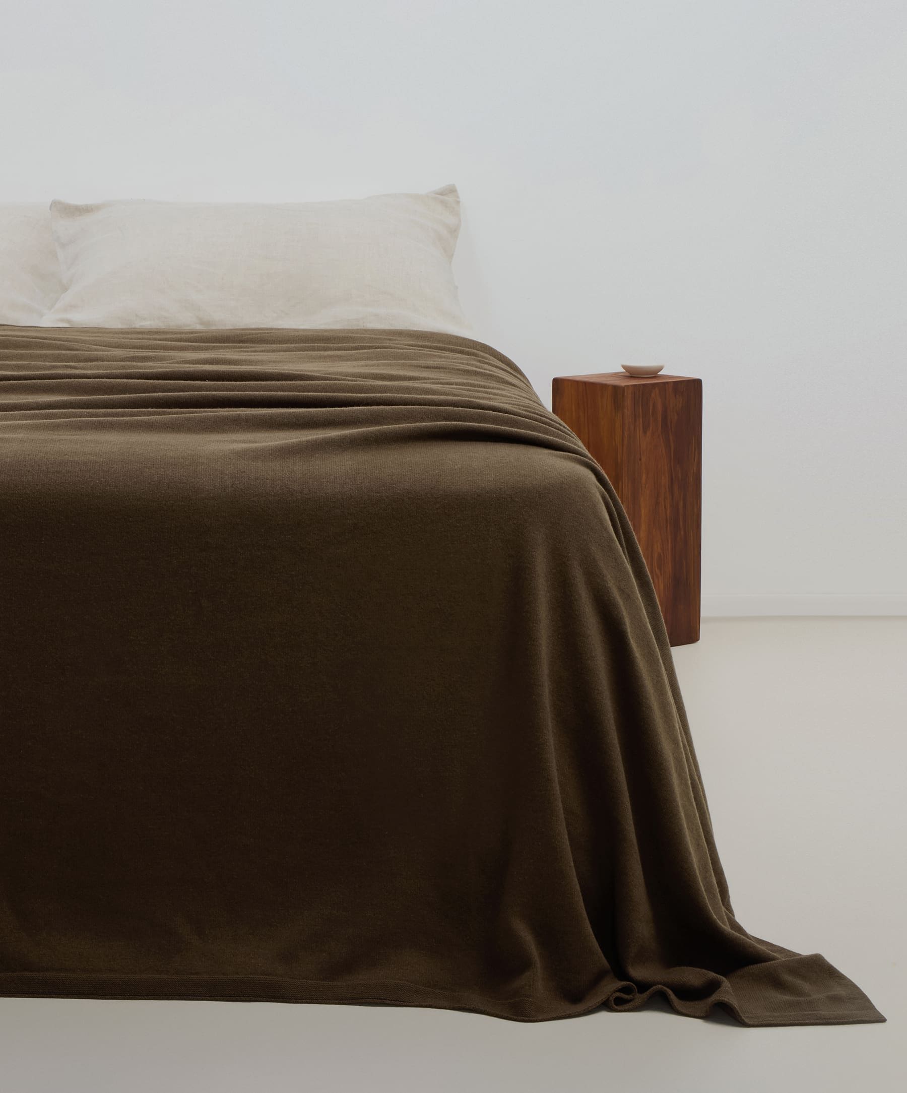 Brown blanket draped over a bed with a wooden nightstand in a minimalistic room.