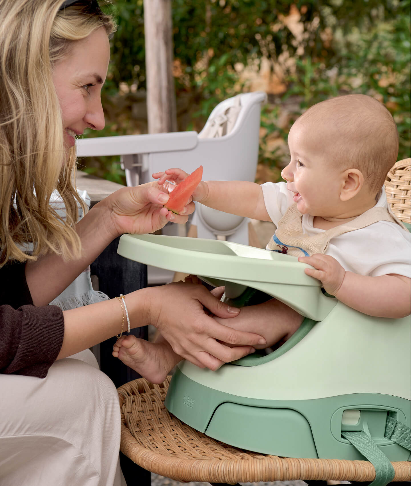 A mother interacts with her happy baby in a high chair.