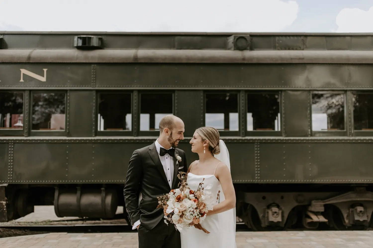 Bride and groom holding bouquet in front of old train