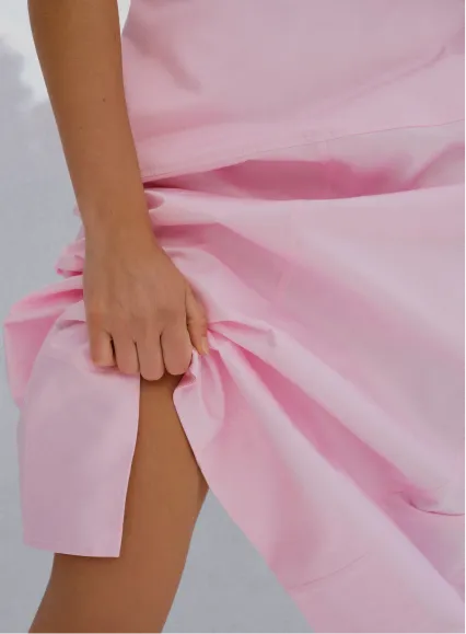 A person holding a pink dress, revealing part of their leg.