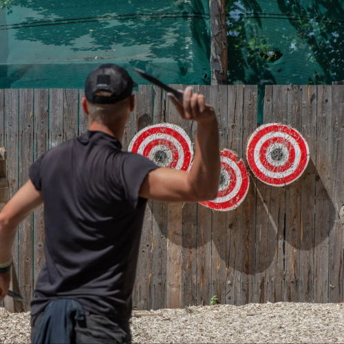 Person throwing an axe at colorful target boards outdoors.