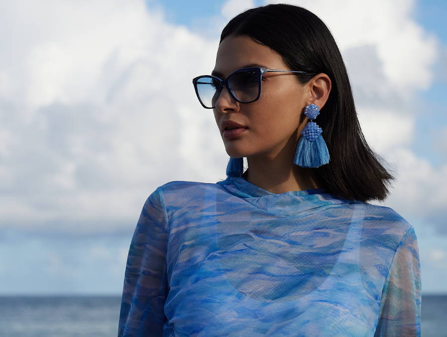 Woman wearing blue mesh hoodie cover up over bathing suit with blue sunglasses and earrings by Ala von Auersperg