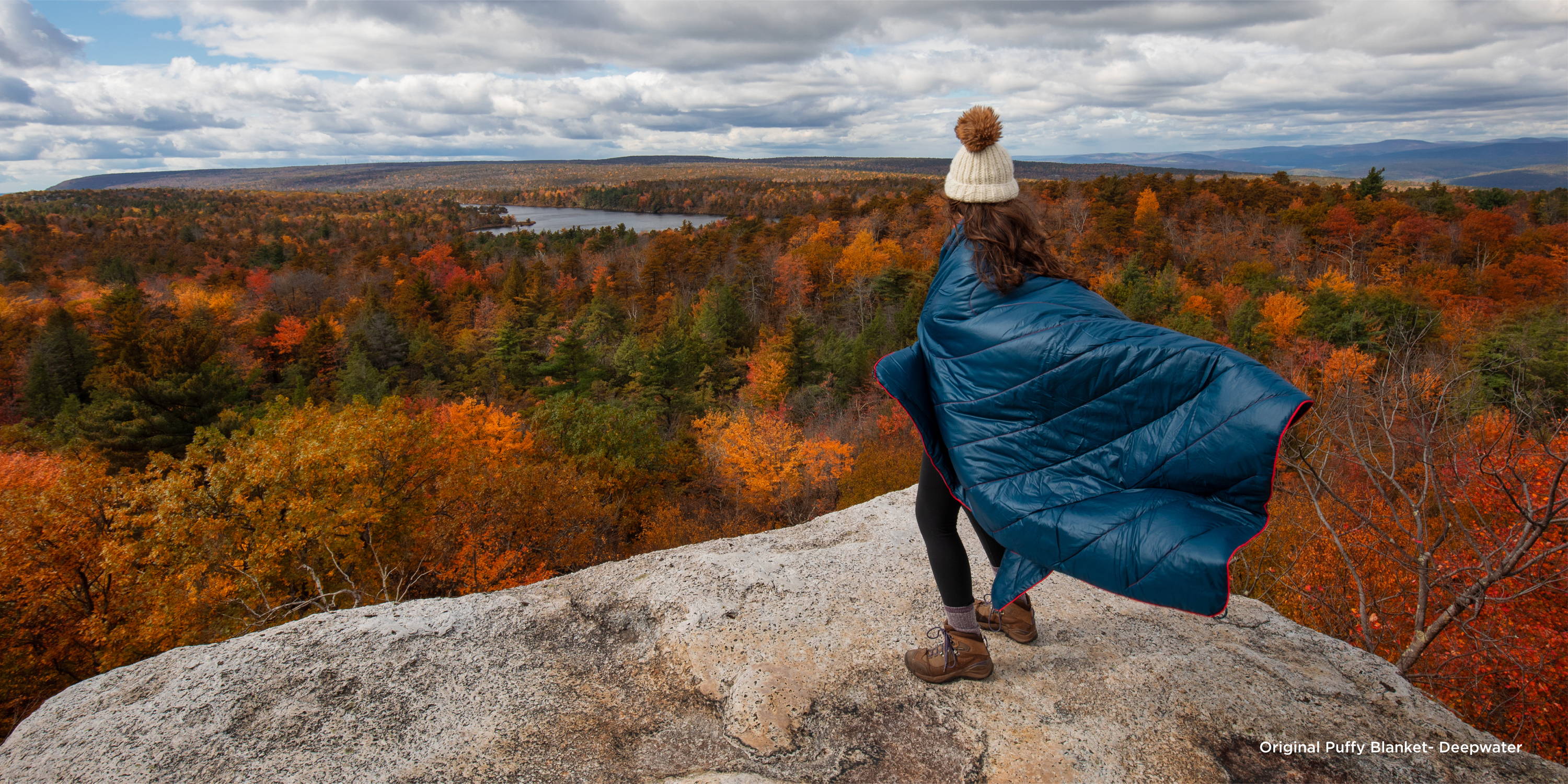 Teen wrapped in Original Puffy Blanket overlooking forestscape