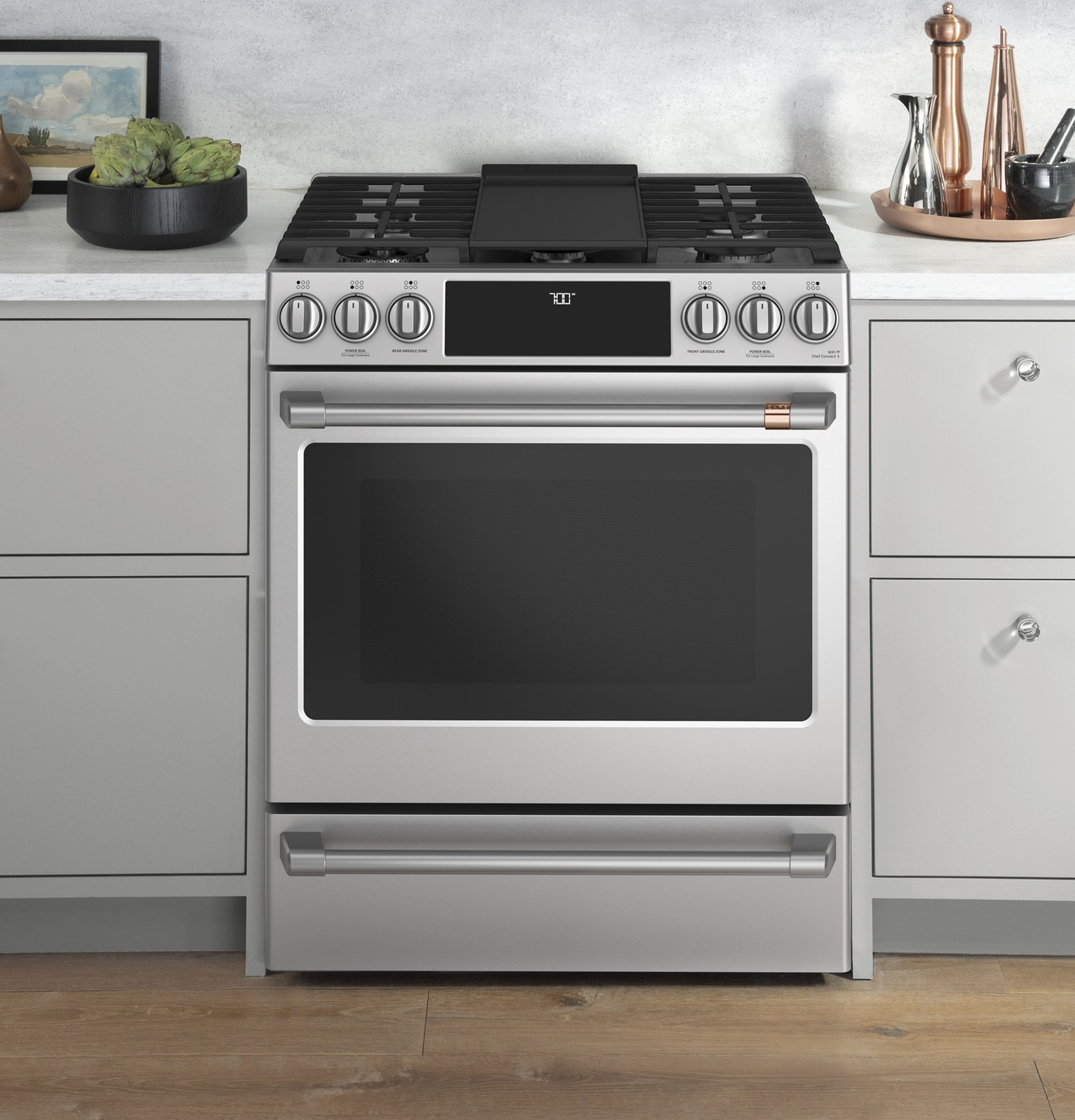 A modern stainless steel kitchen stove with a black top and wooden floor.