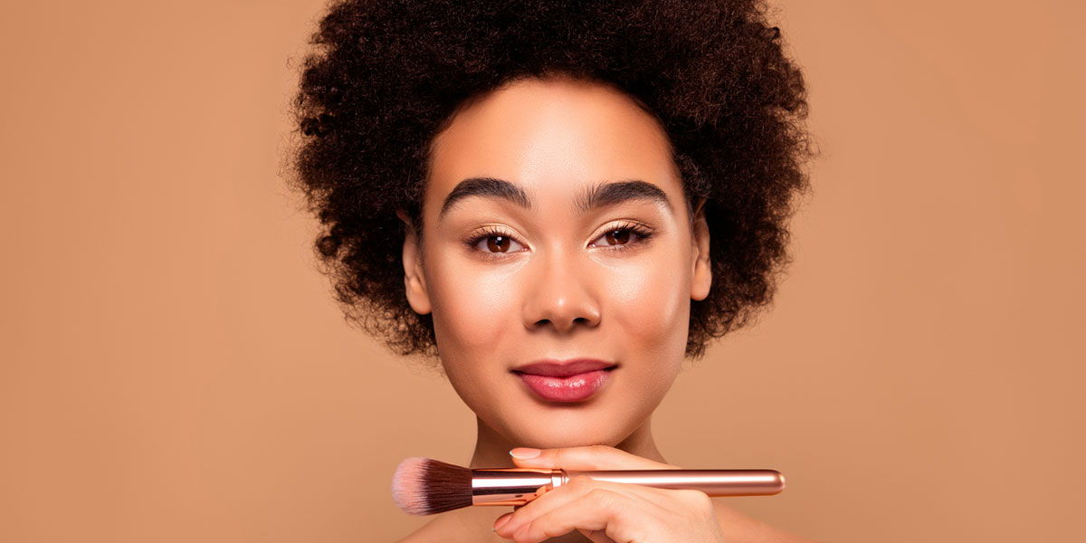 Woman with curly hair holding a makeup brush against a warm background.