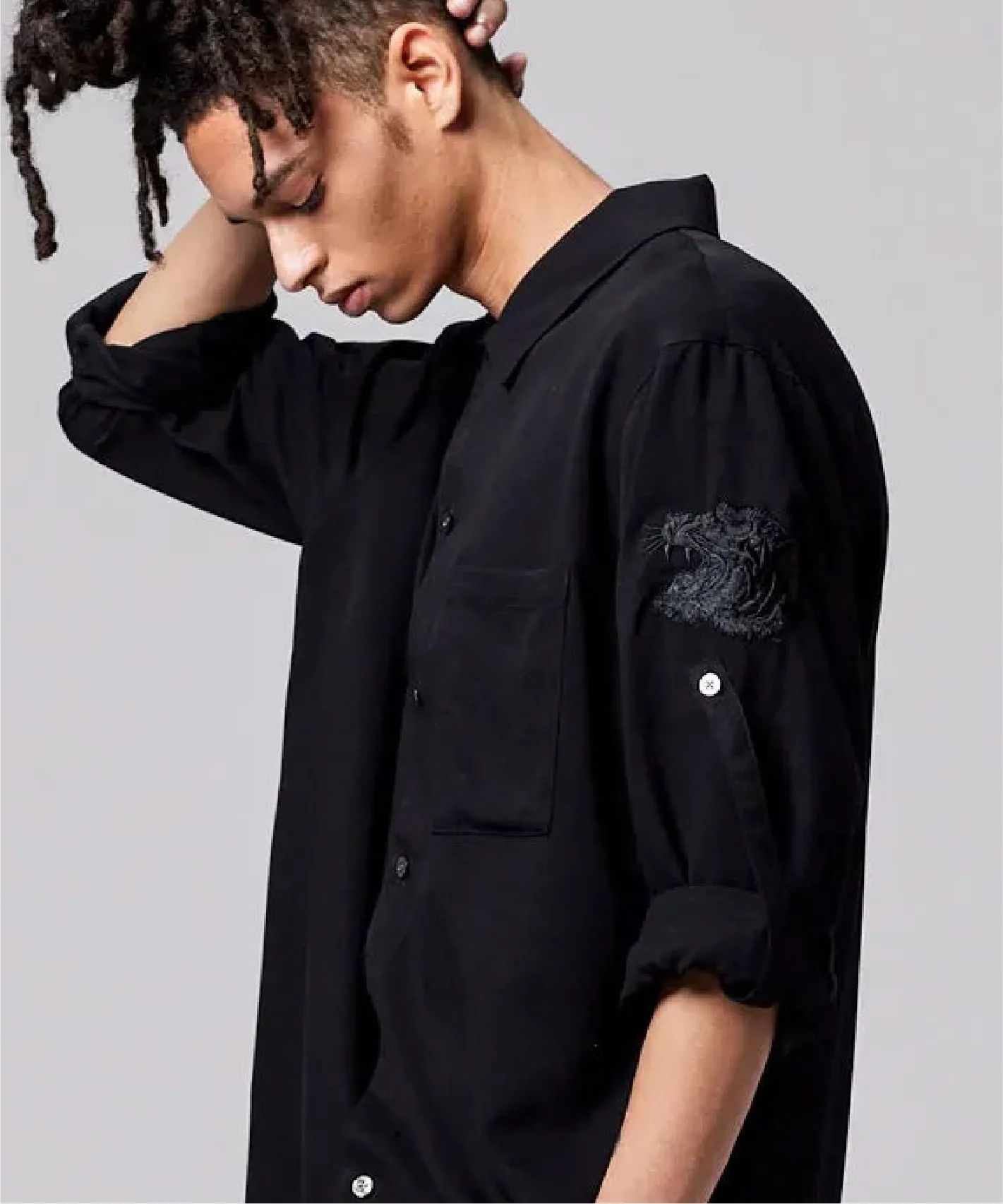 A person with dreadlocks wearing a black button-up shirt, looking down.
