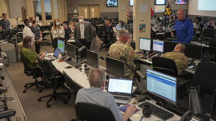 A busy operations center with personnel at computers and a speaker addressing the group.
