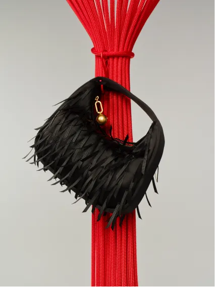 Black fringed handbag hanging from a red pole.
