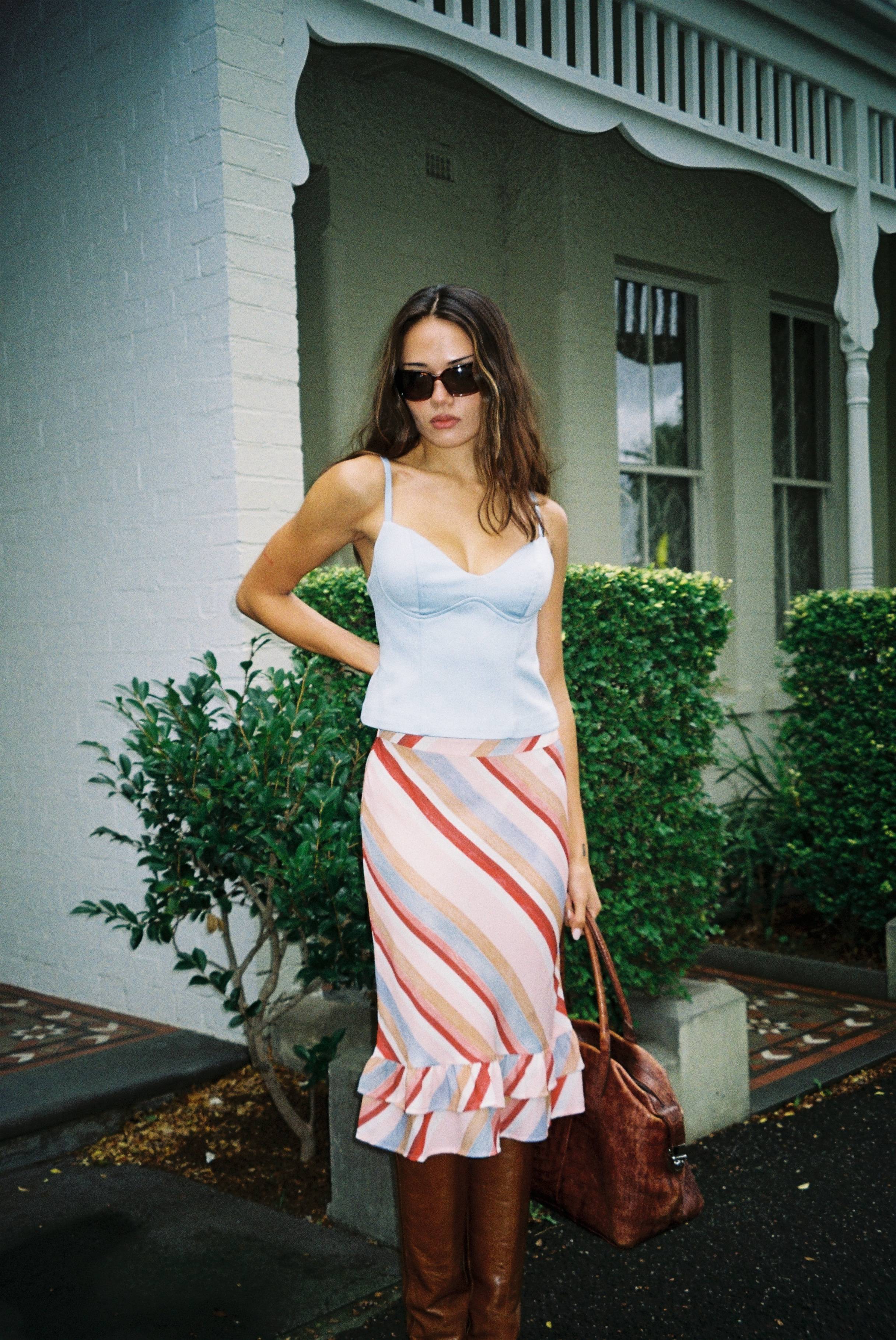 Woman in a stylish outfit standing outside a building with greenery.